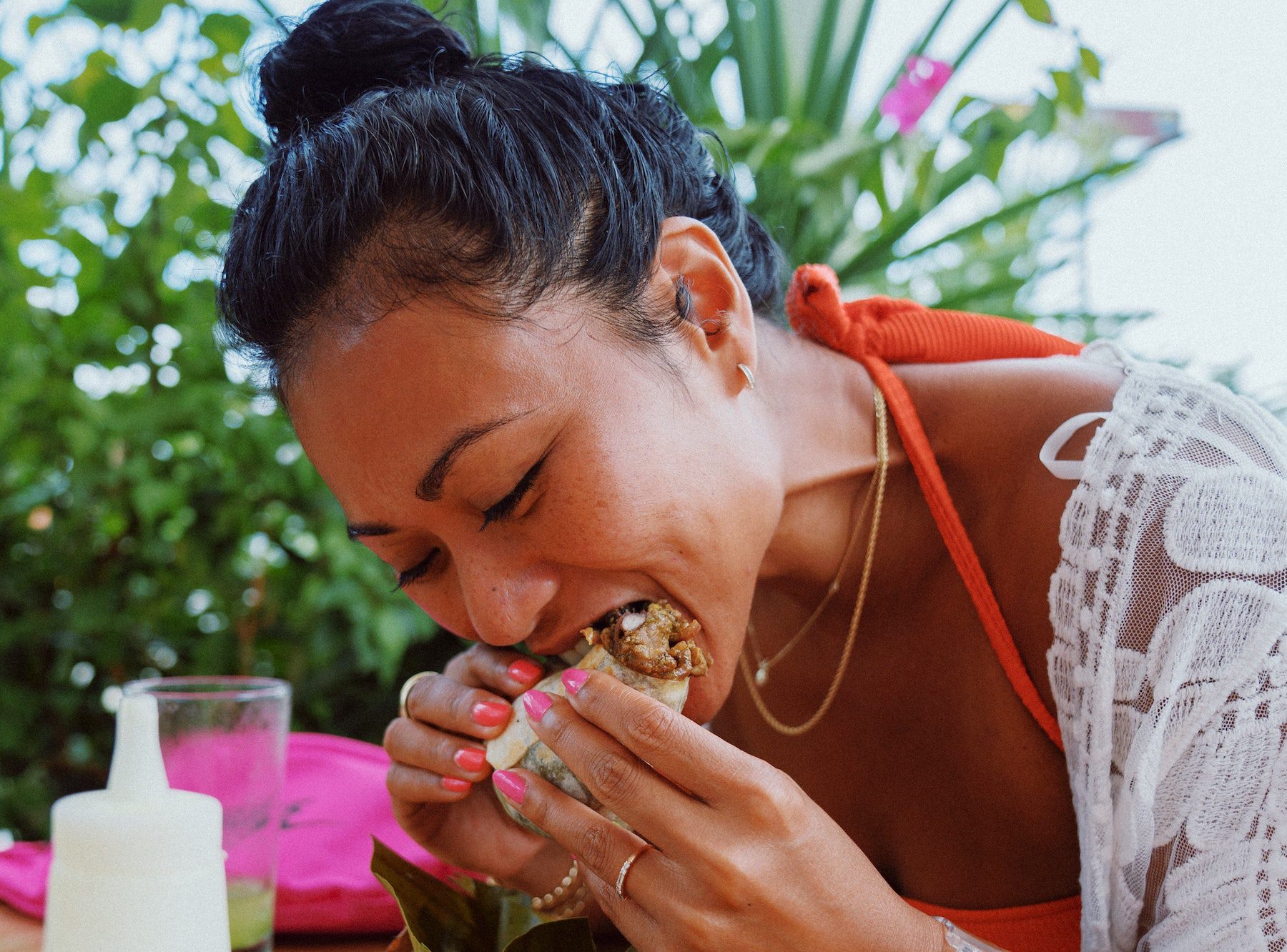 Pretty Asian woman bites into burrito at outdoor restaurant. 