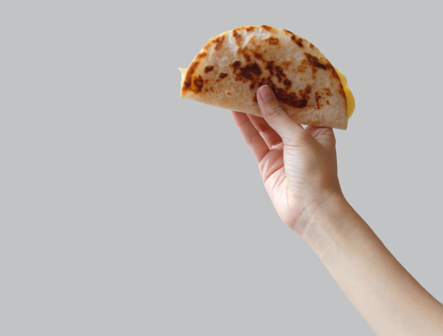 Unseen person holding a taco in the air against gray background. 