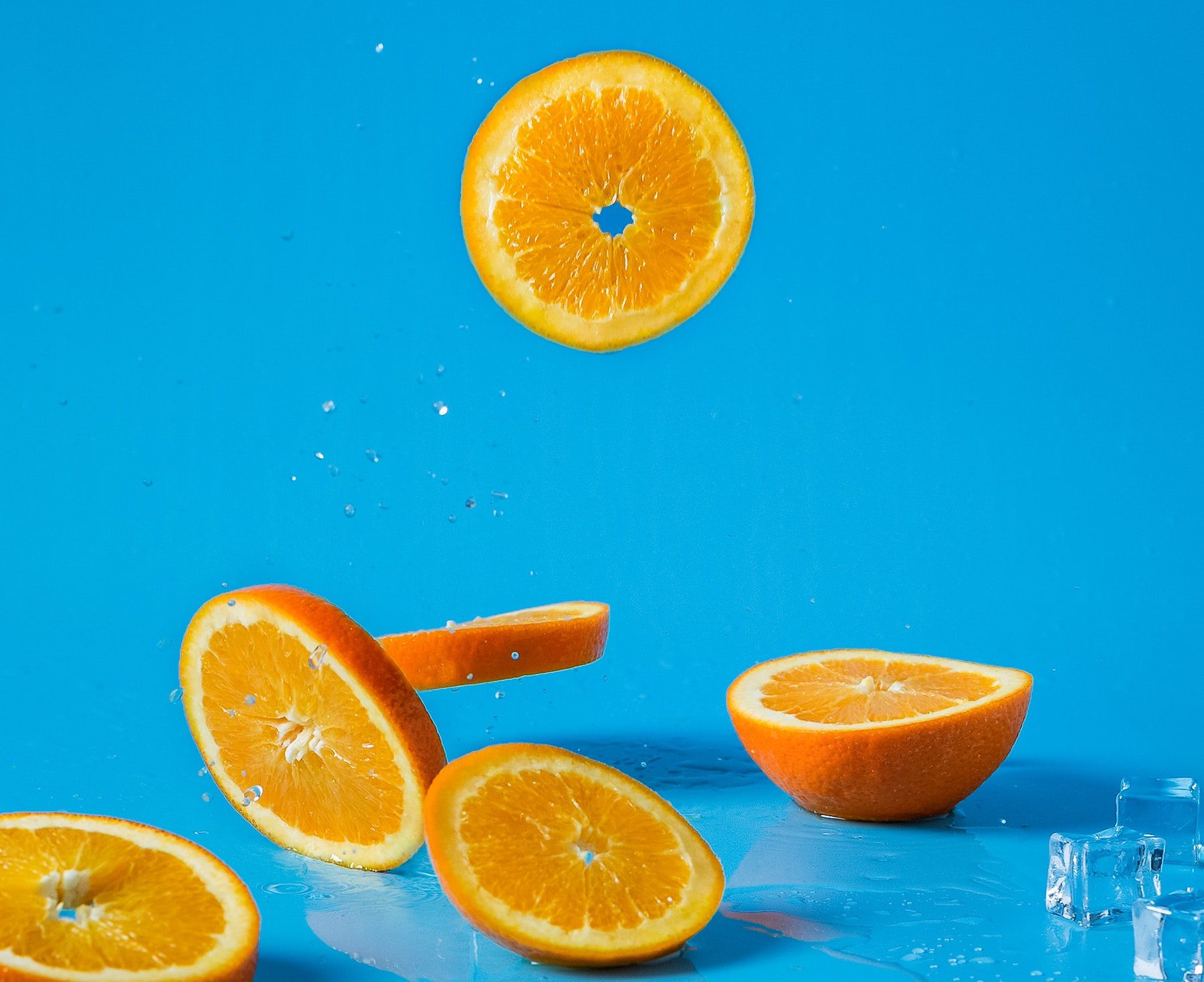 Orange slices against a bright blue background falling and scattering on a blue tabletop.