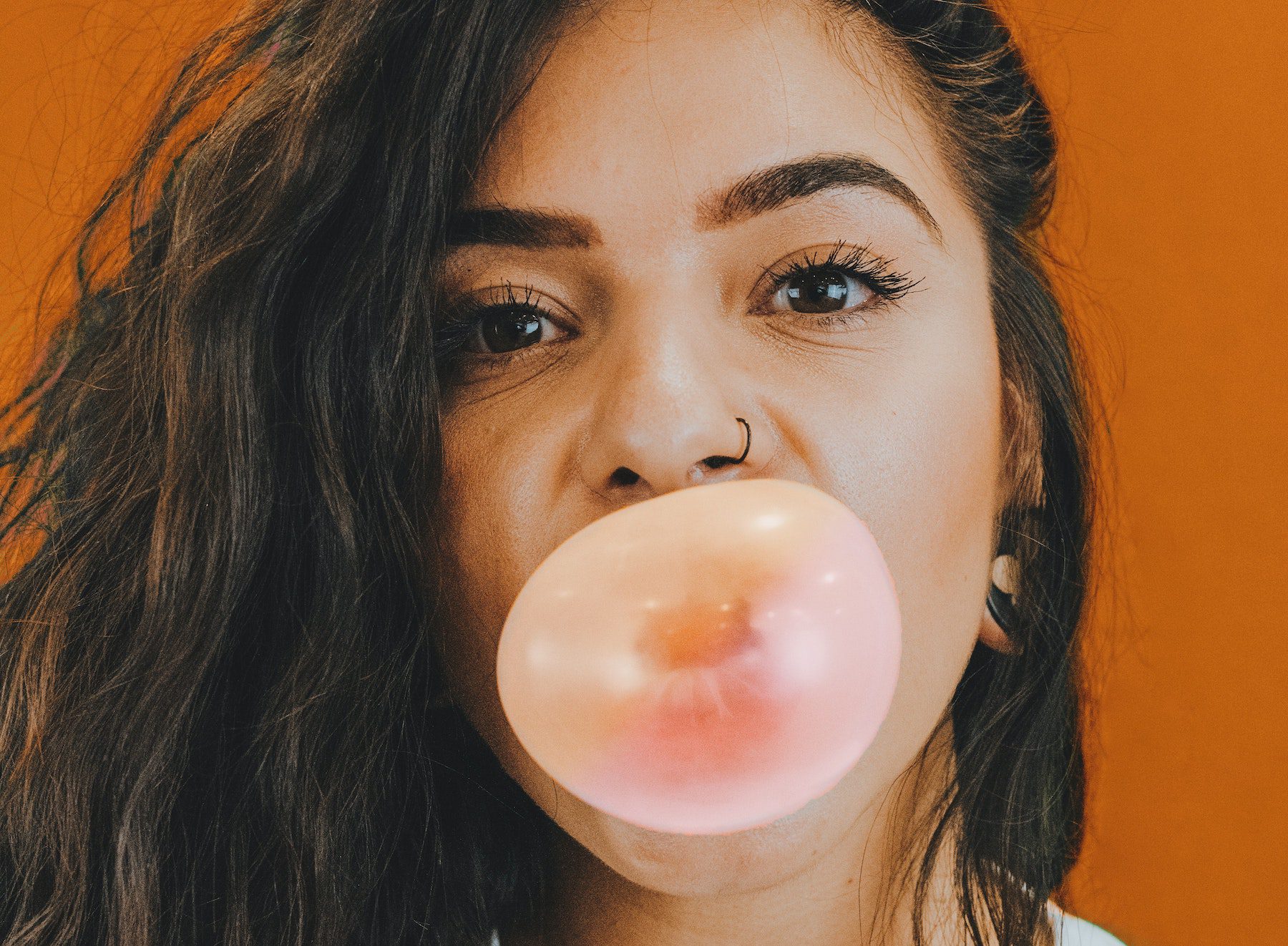 Pretty brunette woman blowing a bubble with gum against burnt orange background. 
