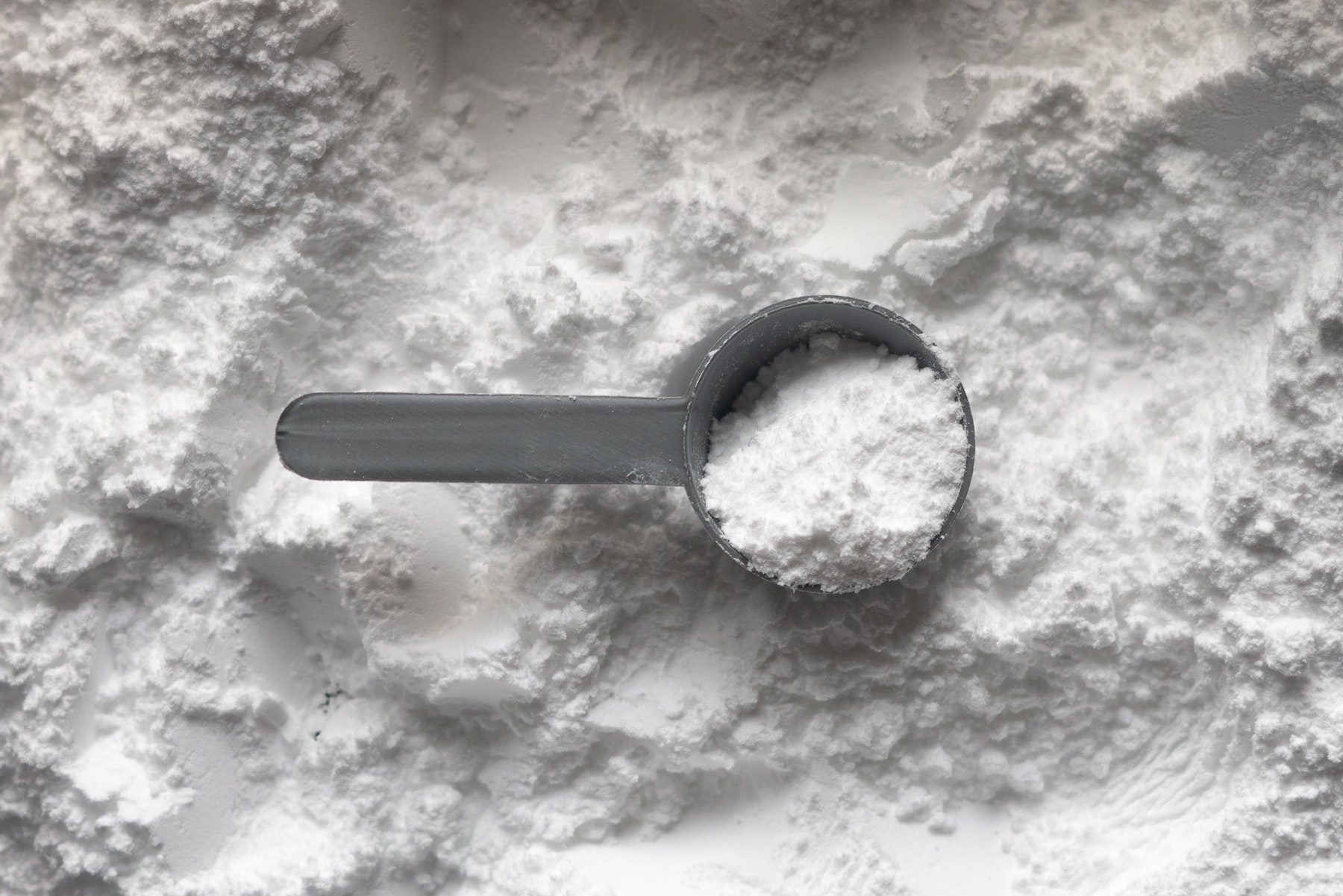 A scoop of white protein powder on a larger pile of protein powder. 