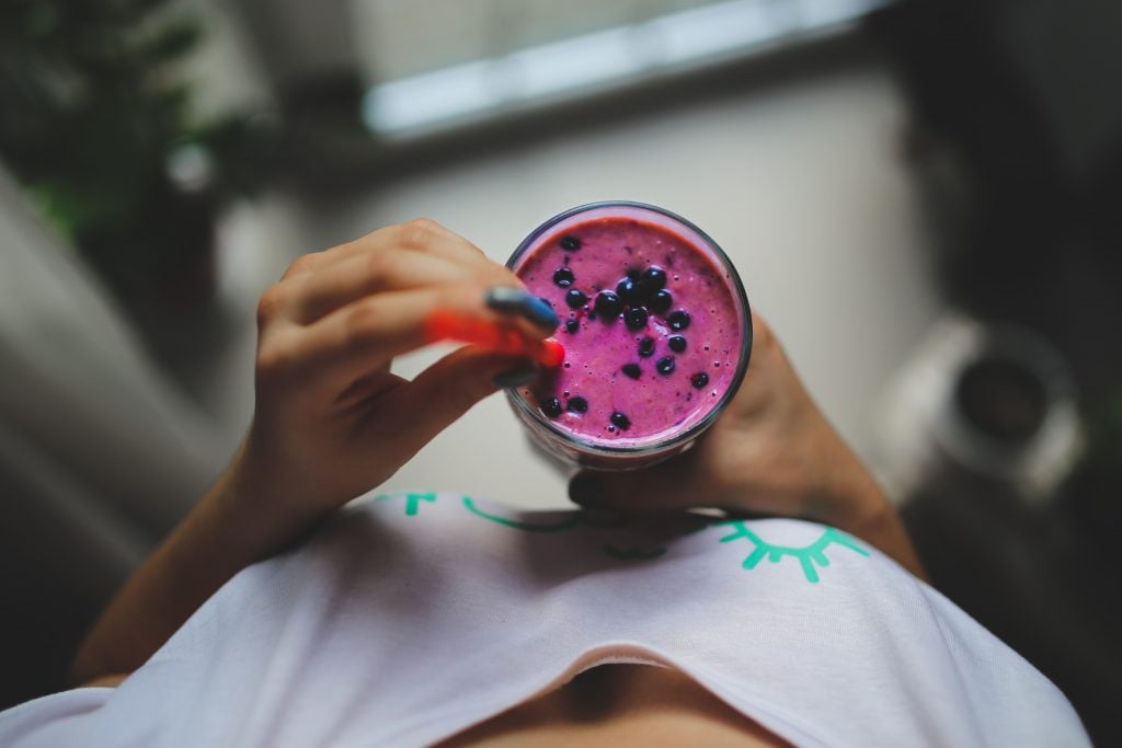 POV from an unseen woman looking down at a breakfast smoothie, purple and filled with blueberries with a red straw.