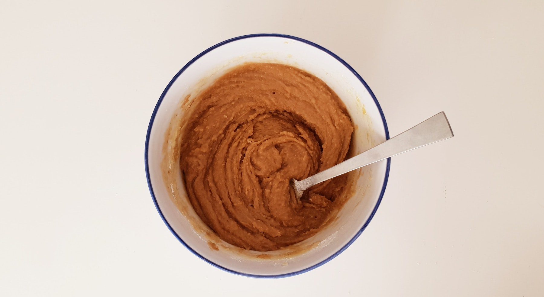 Natural ground peanut butter in a ceramic dish with spoon.