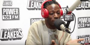Freestyle rap artist Joey Bada$$ with red headphones sitting in a radio booth with a mic.