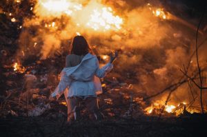 A young girl stands before carnage and fire reminiscent of the apocalypse.