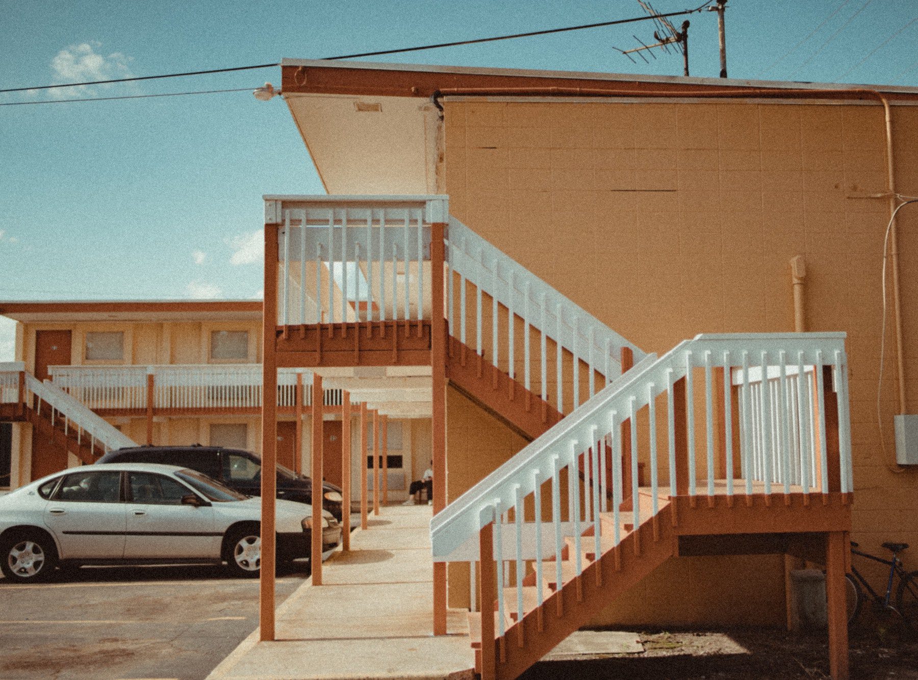 The outside of a two-story motel with light orange paint and white stair railings.