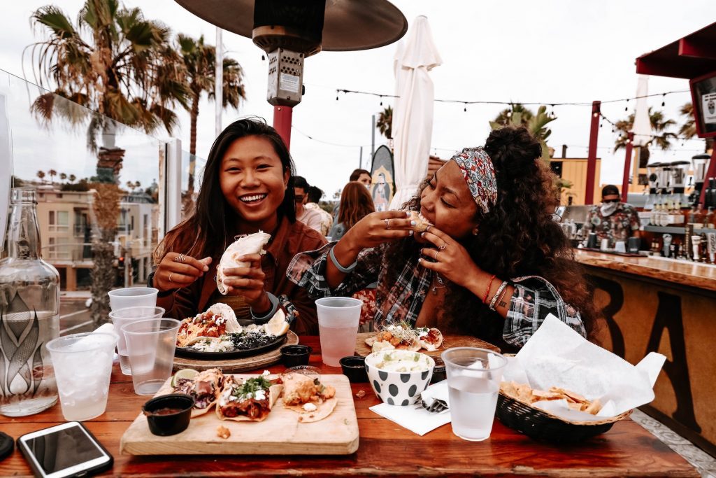 Two women enjoy Taco Tuesday at one of San Diego CA's Mexican restaurants, smiling at a table full of food and drinks.