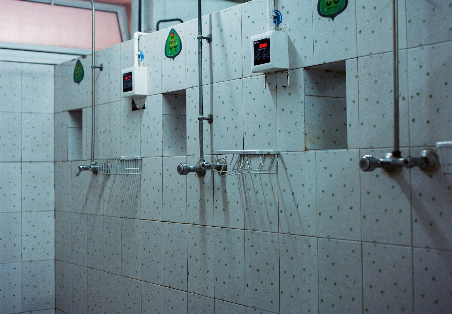 A row of showers in a gym or camping facility with white tiles.