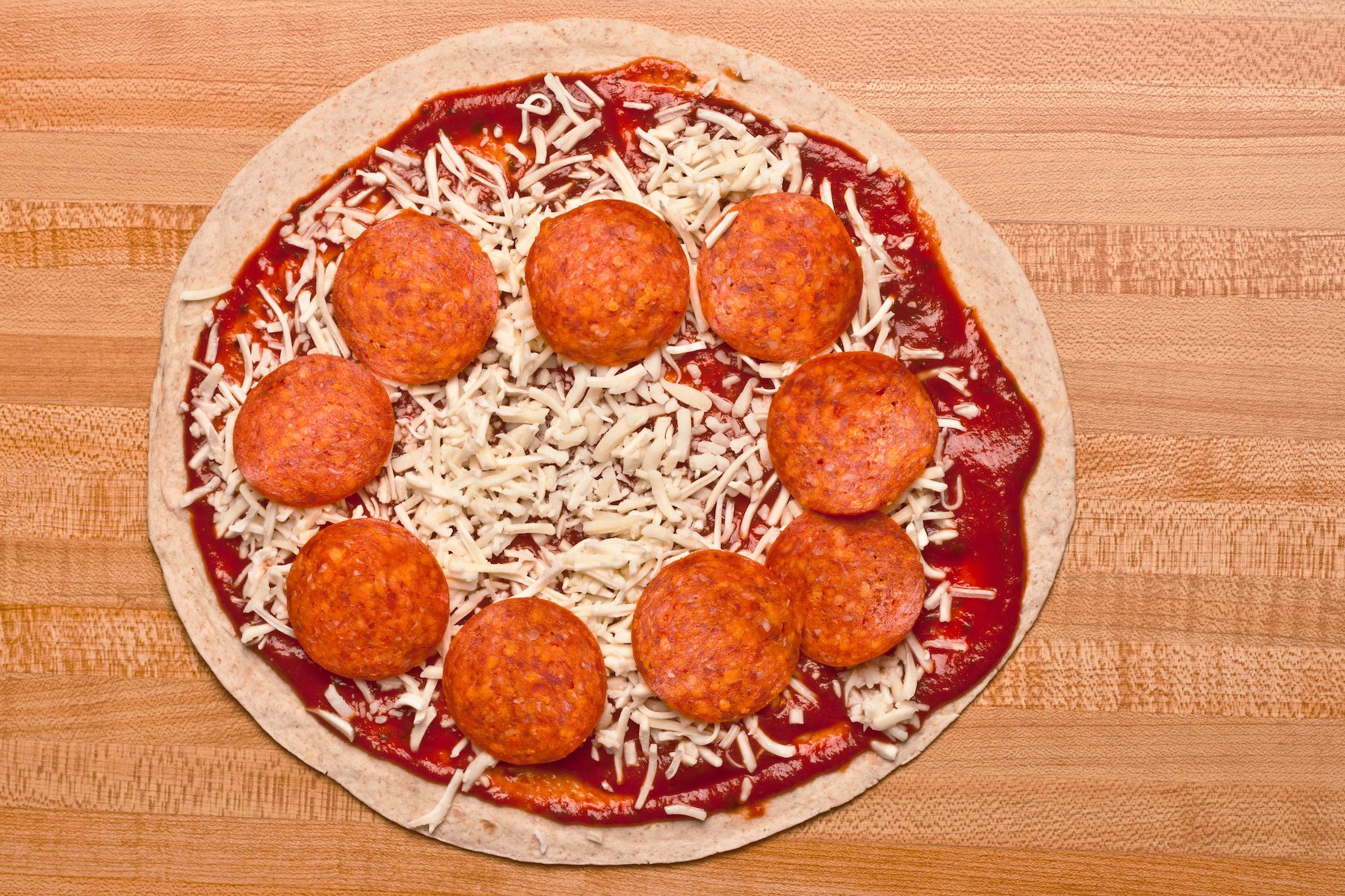 Tortilla Pizza topped with sauce, cheese, and pepperoni on wooden countertop before baking. 