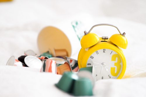 A bright yellow alarm clock amidst scattered objects on a white bed. 