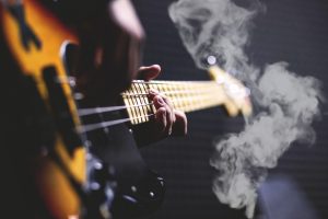 An unseen guitarist playing songs while marijuana smoke rolls in front of instrument.