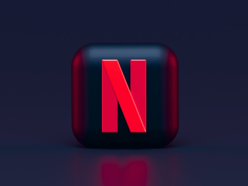 Netflix app logo in black and red casting a glow on a reflective black surface.