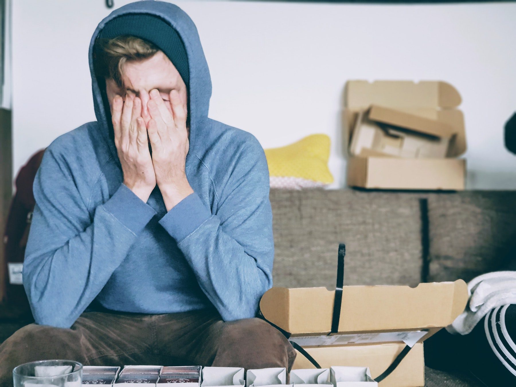 Young man under stress wearing a blue hoodie with hands over eyes.