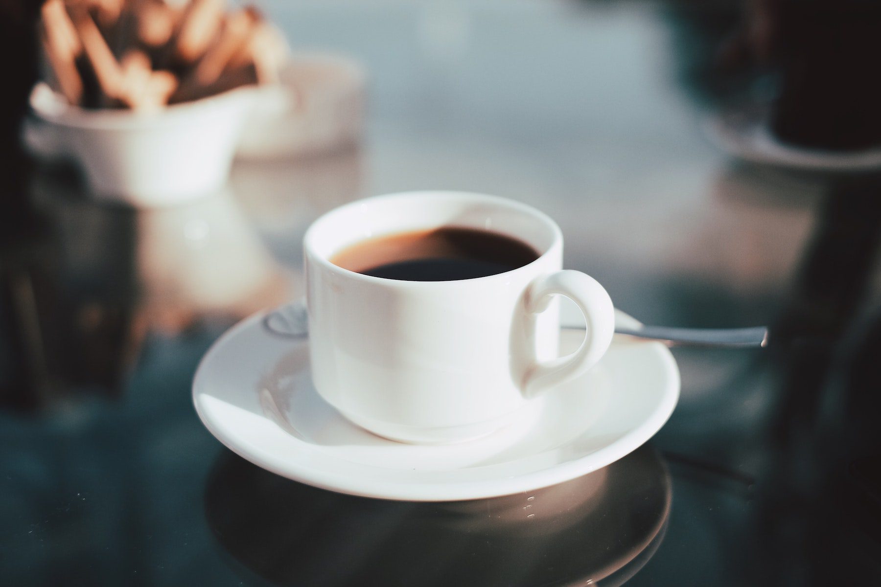 Coffee in small white ceramic cup on saucer with background blurred.