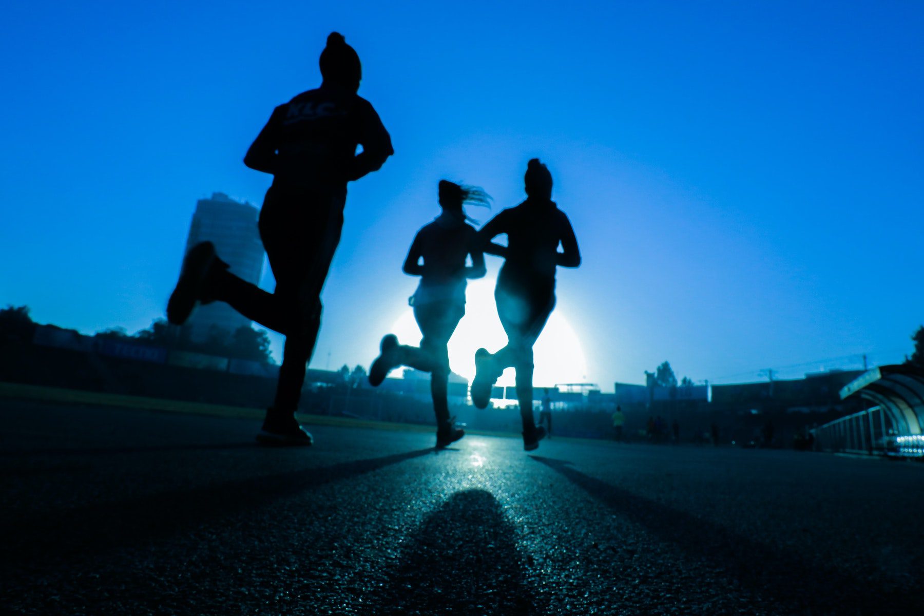 Three women jogging in late evening, silhouettes against blue sky.