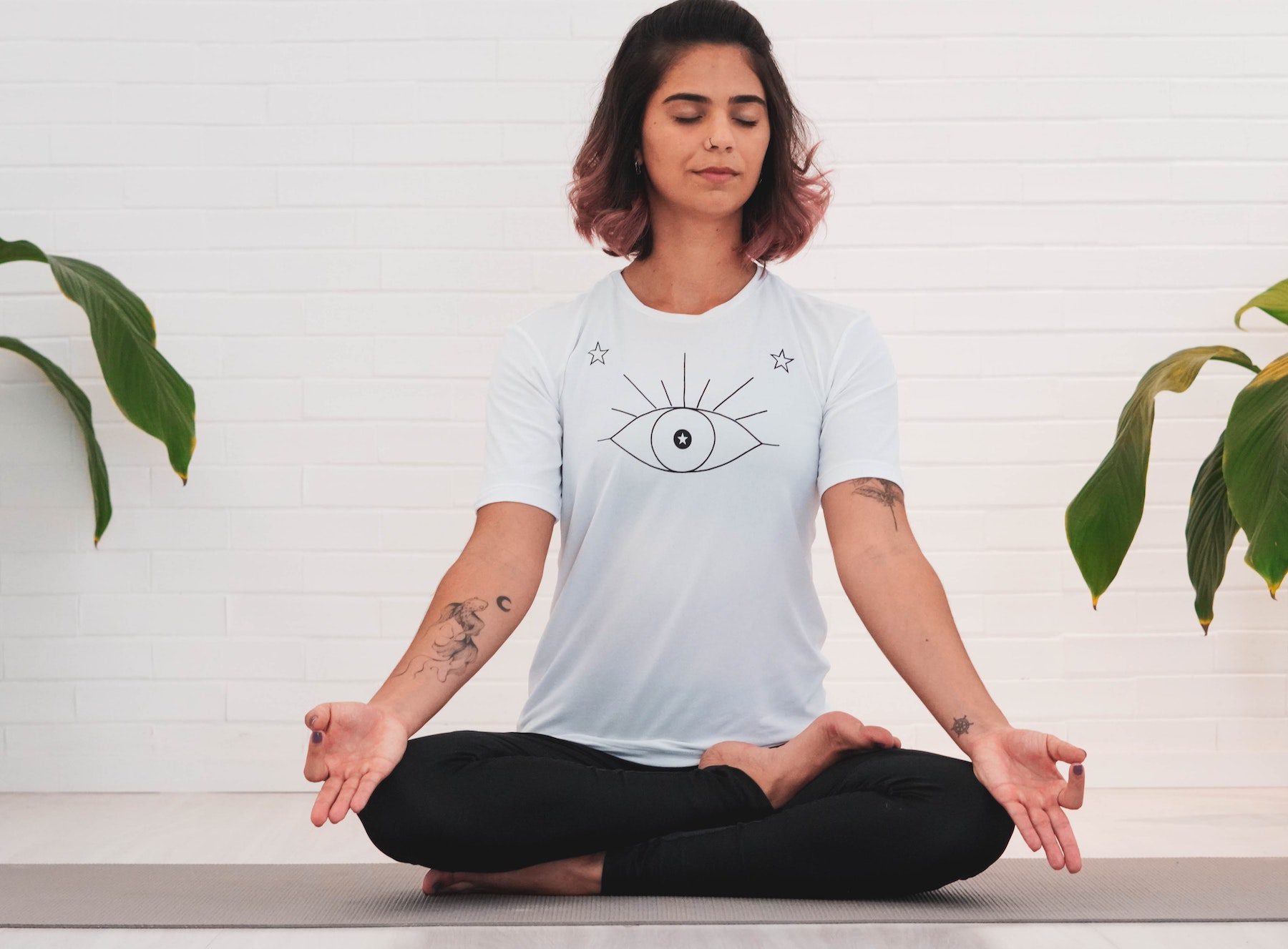 Peaceful and calm woman in white tee and black pants meditating while sitting cross-legged.