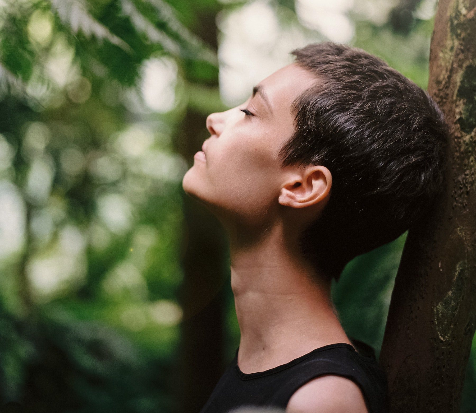 Woman with pixie cut leaning on a tree and breathing peacefully.