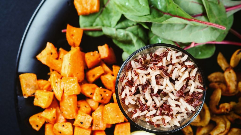 Vegetarian meal with wild rice, greens, and sweet potatoes in a dark bowl.