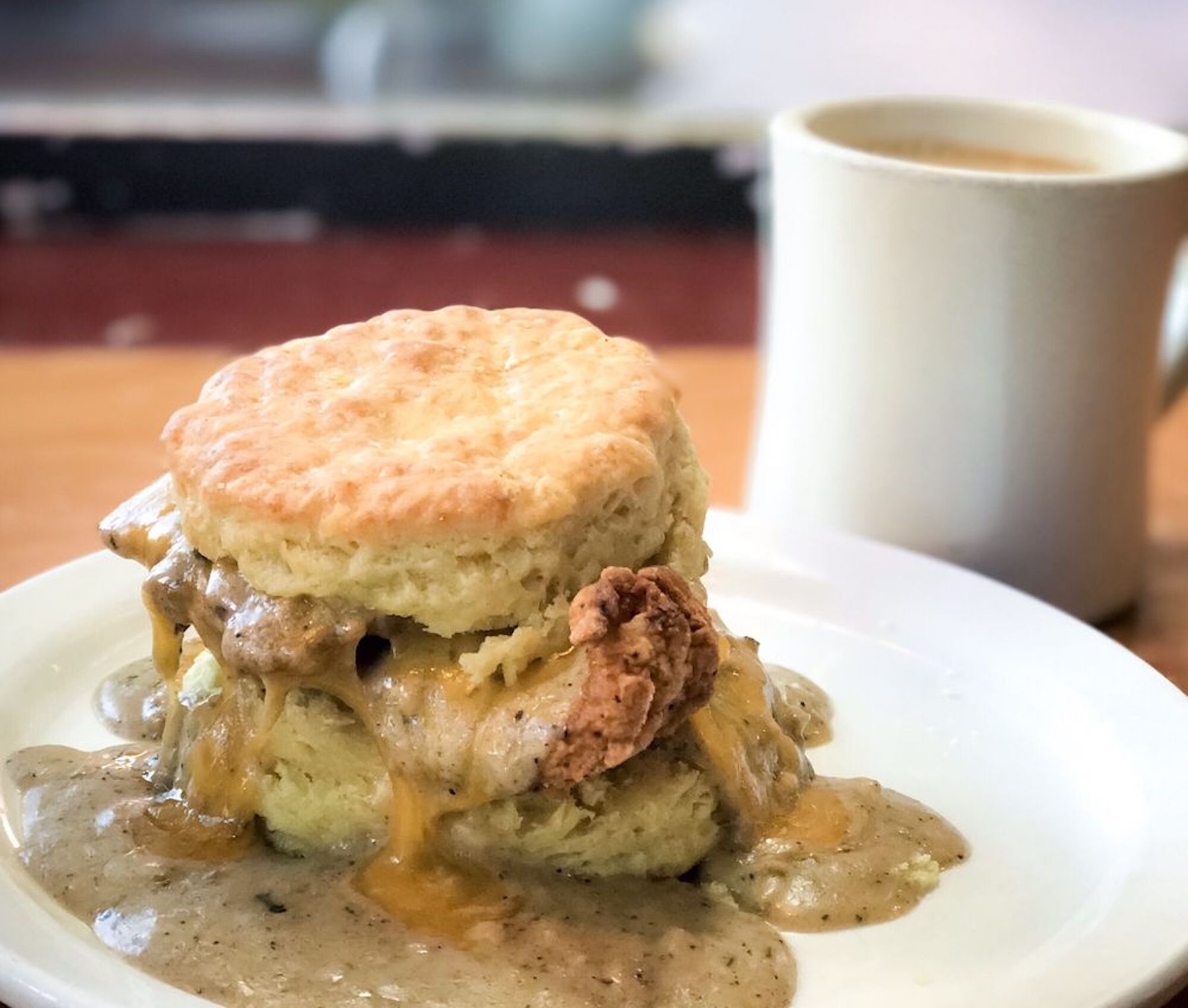 Item menu The Reggie from Pine State Biscuits, a fresh biscuit covered in gravy with a cup of coffee in the background.
