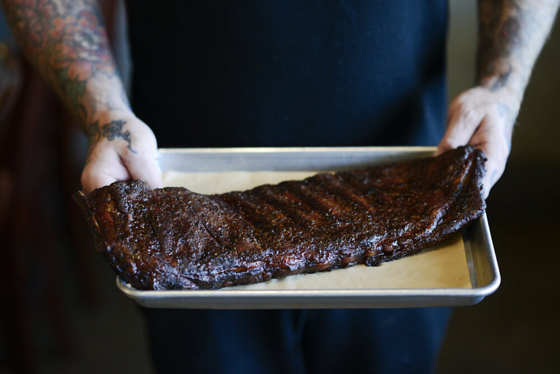 Person in black shirt holding tray with a rack of barbeque ribs.