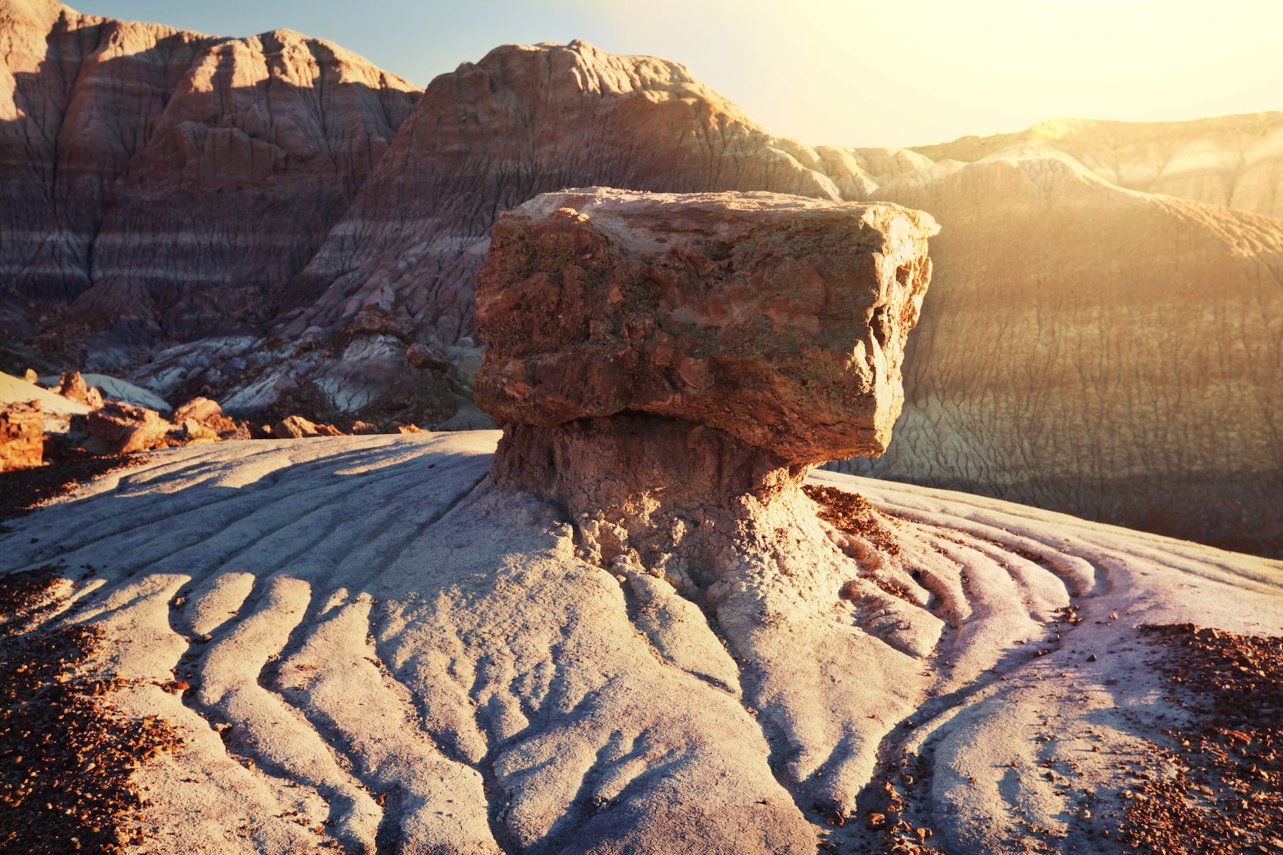 A lone rock formation sits in the foreground with large cliffs shown in the background at Petrified Forest National Park, Arizona