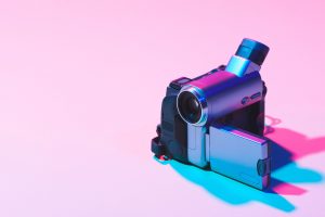 A camcorder set up to film on a pink background casting pink and blue shadows.