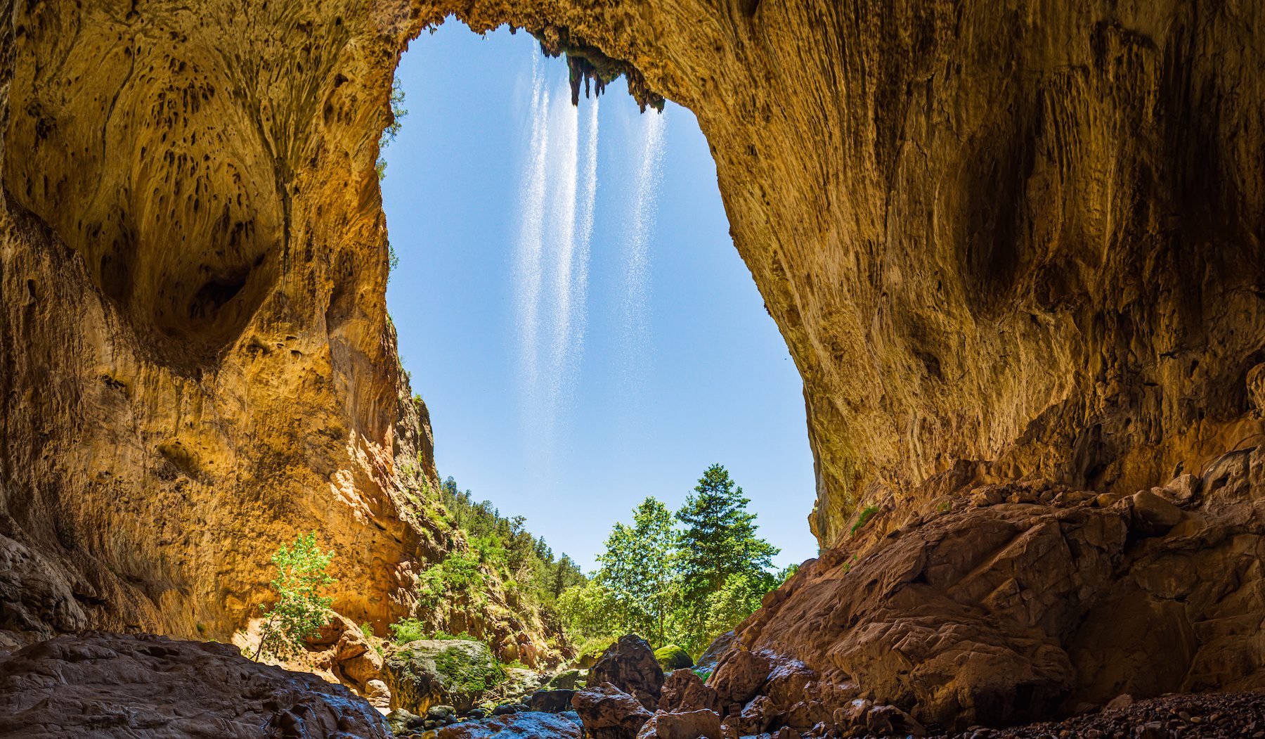 Water cascades from the top of the entrance of the tunnel where red rock boulders lay at Tonto Natural Bridge, Arizona
