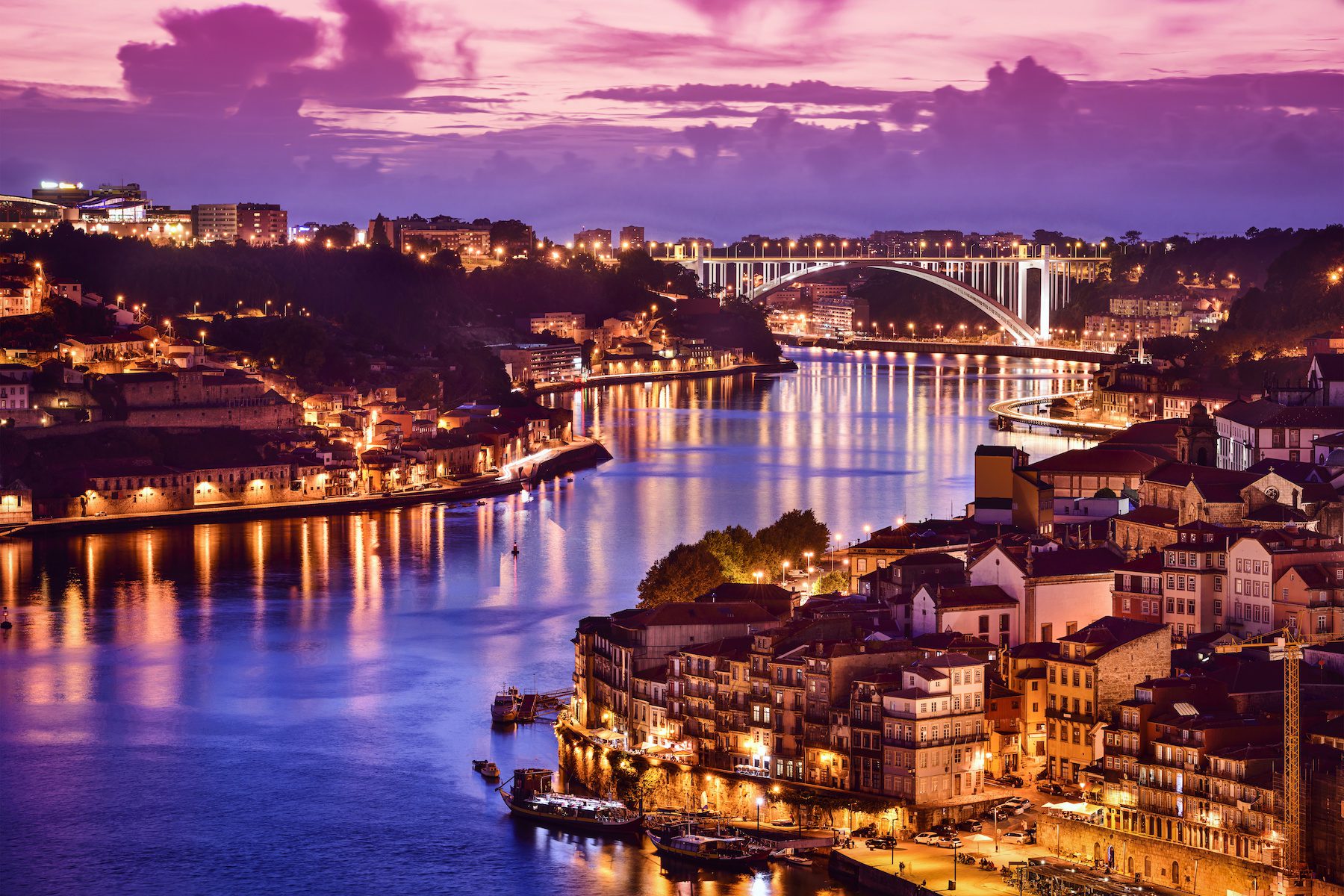 Ribeira District in Portugal on partly cloudy evening as the streetlights from the city light up the river
