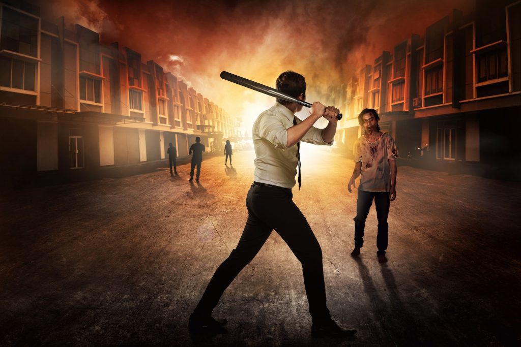 A man with a baseball bat faces off zombies in a burning city.