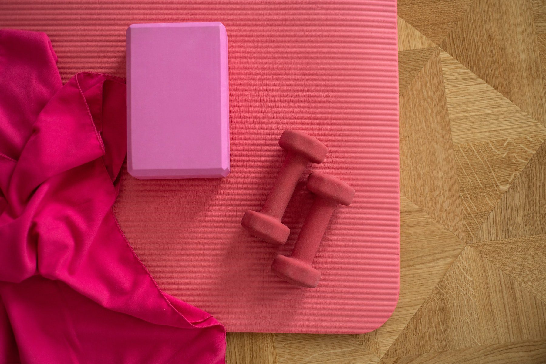 Pink yoga block with a pink towel and red lightweight dumbbells atop a pink yoga mat