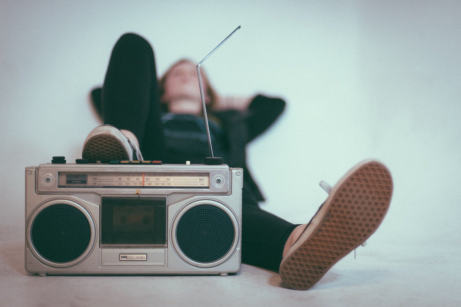 A girl wearing dark clothing laying back with her right foot up against on older style boombox radio