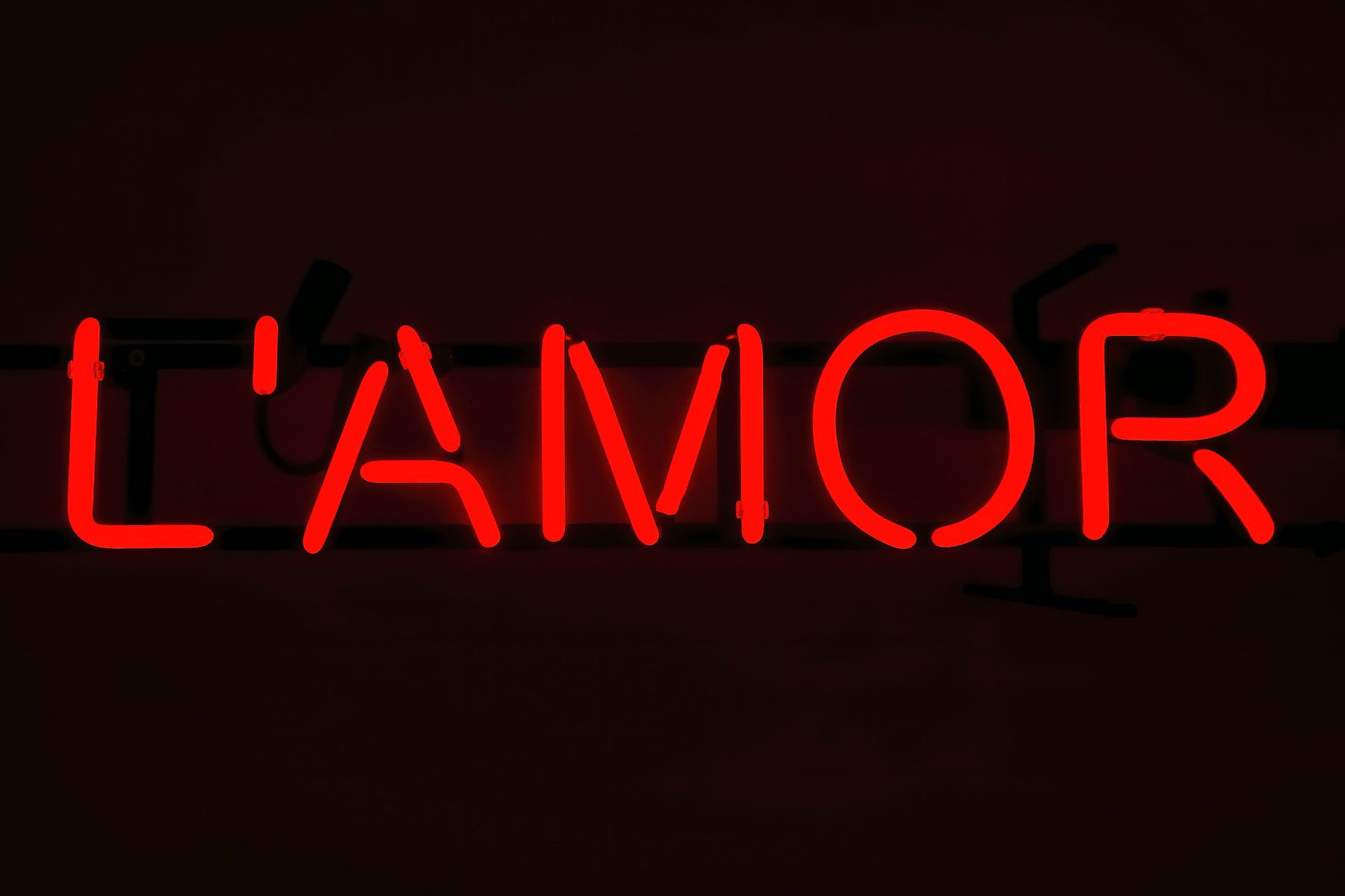 The French word "L'amor" spelled out in red neon light in a dark room