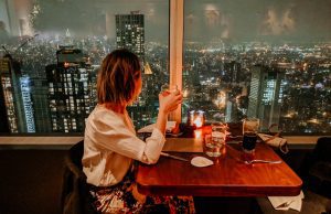 A young woman with short hair enjoying dinner with a view of the New York City skyline.