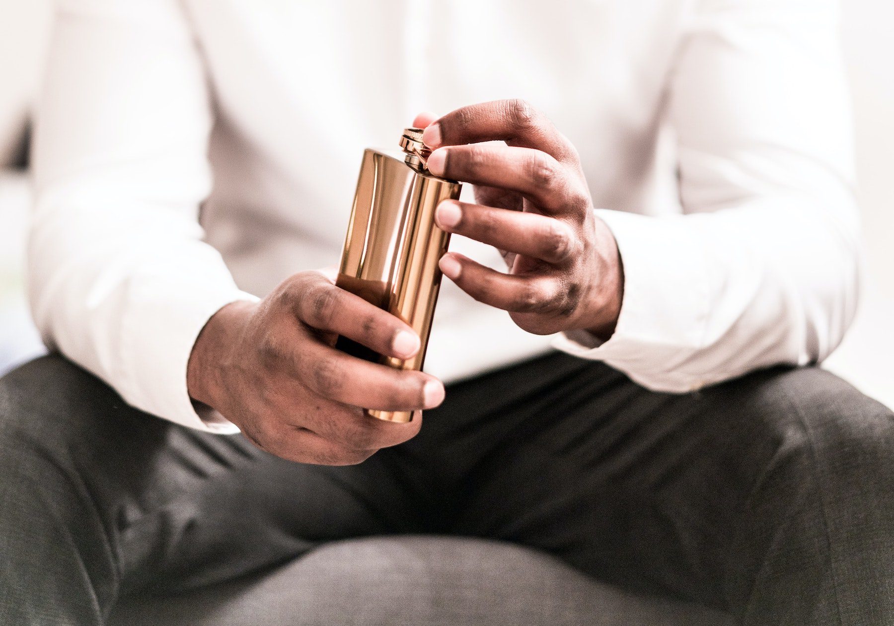 Indian man in black dress pants and white shirt holds a copper flask of alcohol.