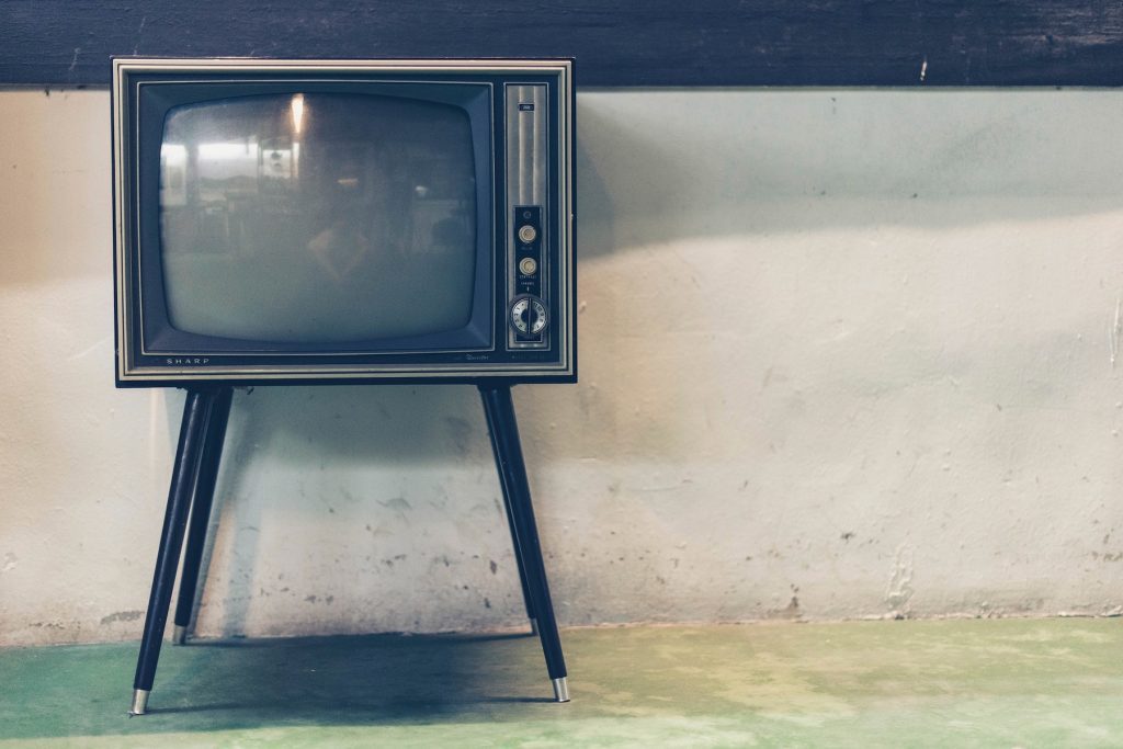 An old-fashioned television set against a bare concrete wall with a blank screen.