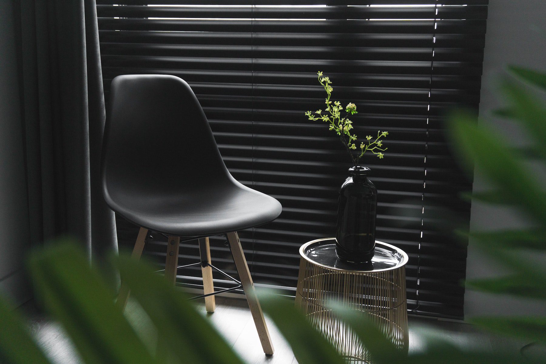 A modern style chair in front of a window next to a side table with a plant in a vase