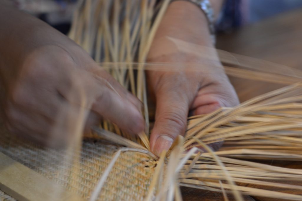 Hands weaving a basket from straw.