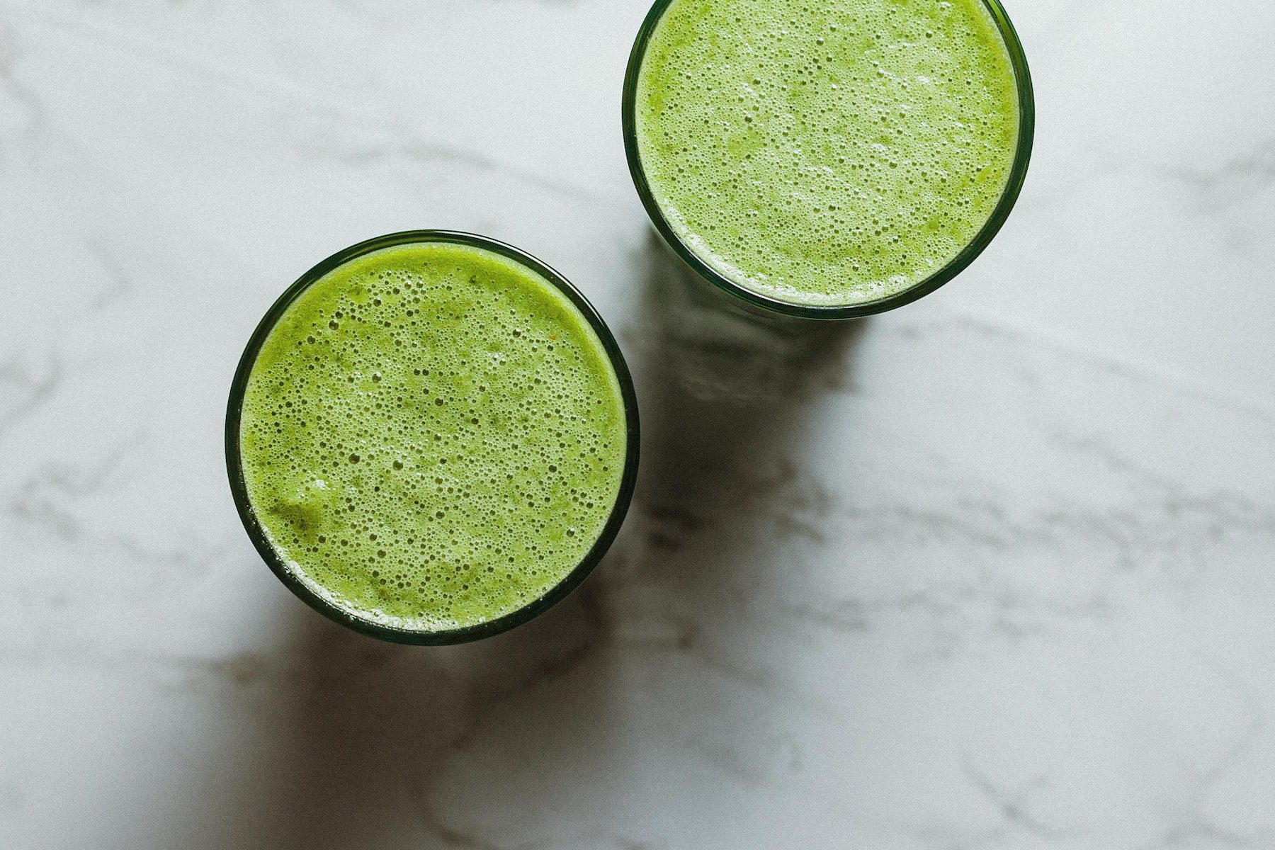Two green smoothies seen from above on a white marble counter.