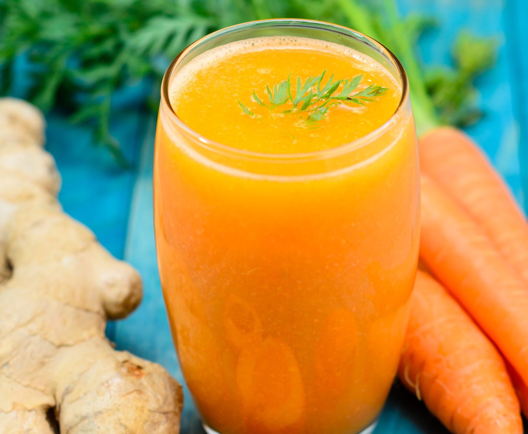 Orange smoothie with ginger and carrots on a blue table.