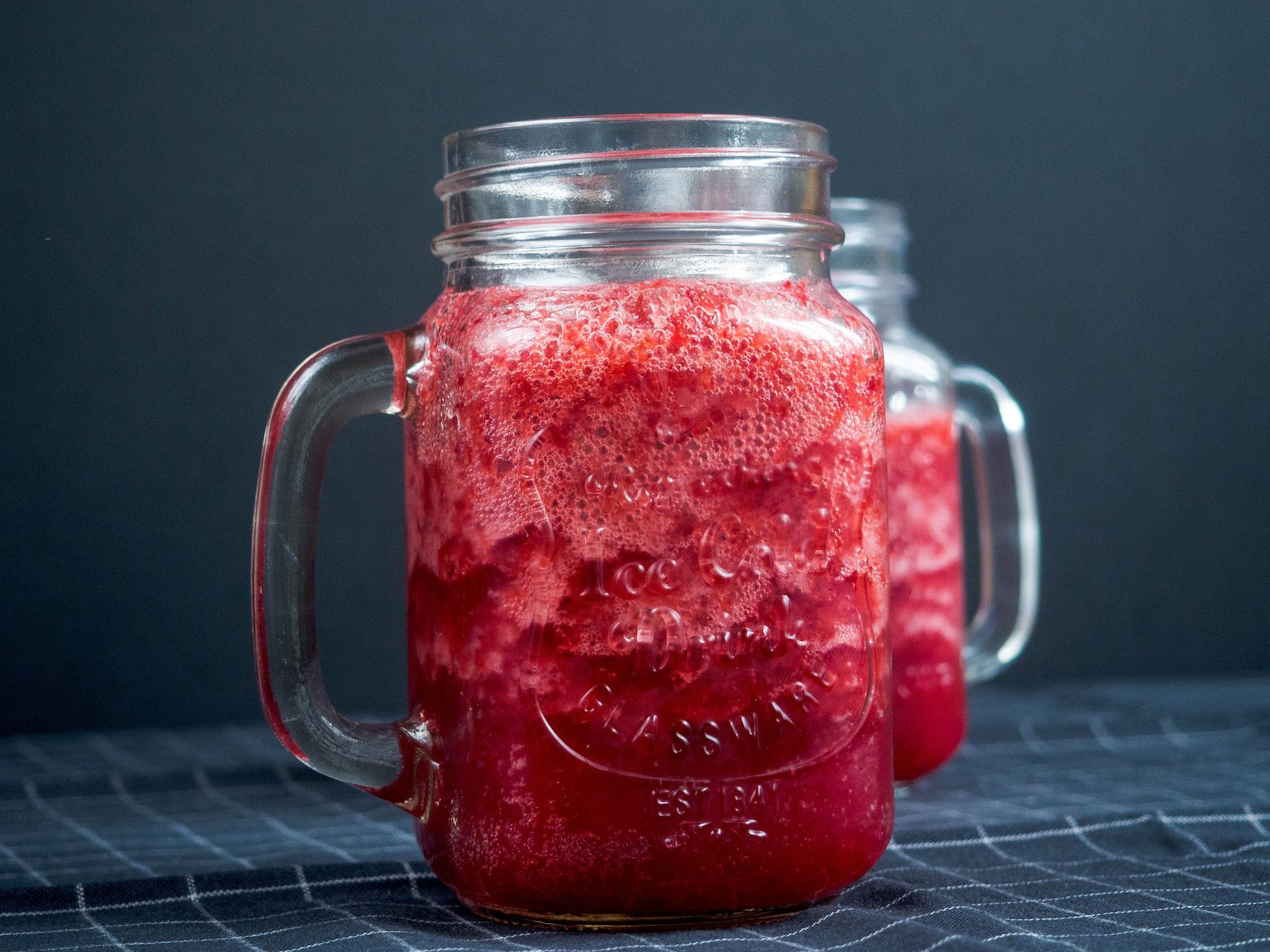 Icy bright red smoothies in mason jar glasses against deep blue background.