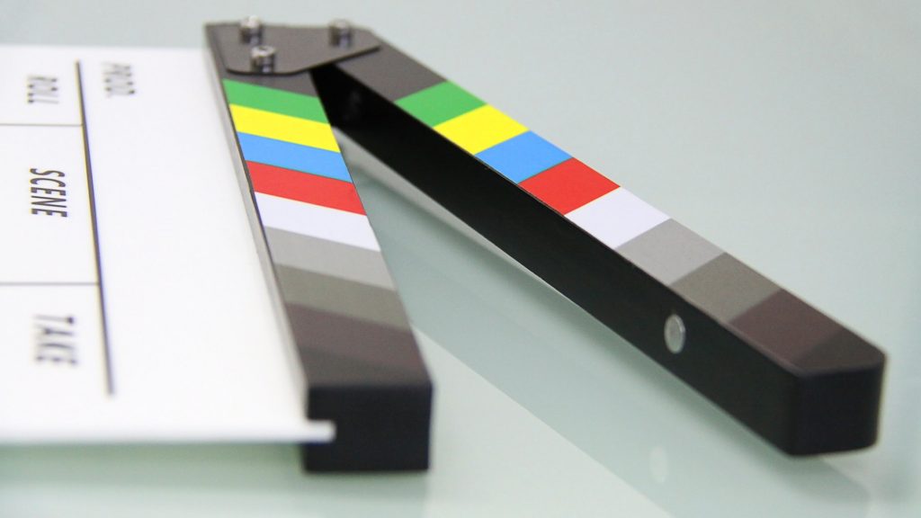 A movie clapperboard lying on a gray reflective table.