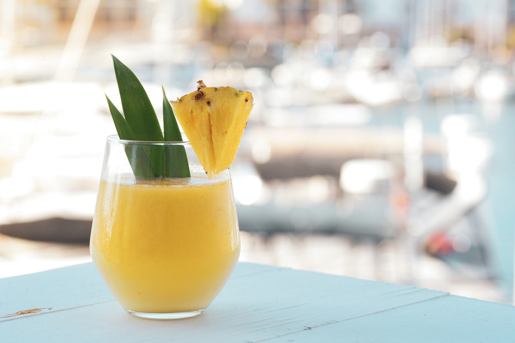 A yellow smoothie on a light blue tabletop, garnished with a pineapple slice and greenery.