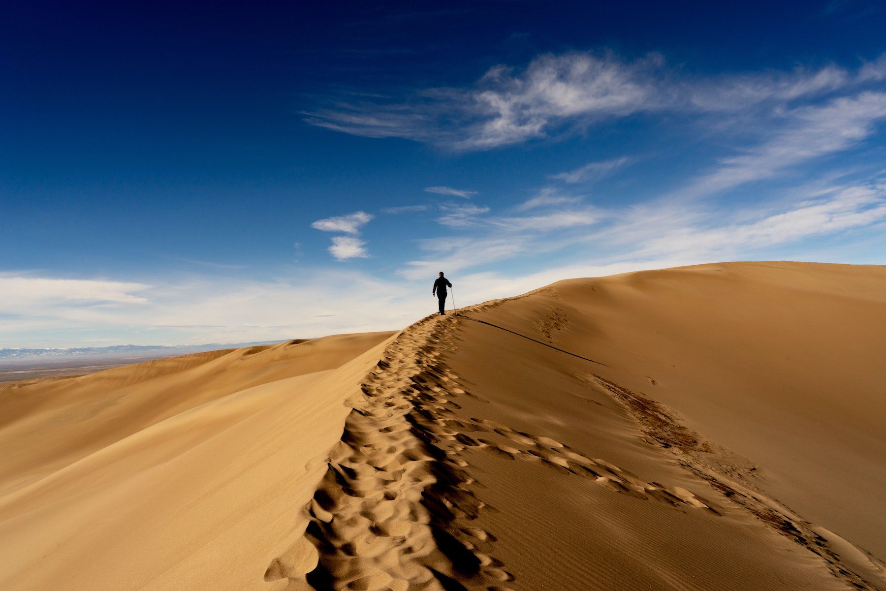 Person in the distance walking along sand dunes at the Great Sand Dunes National Park in Colorado.