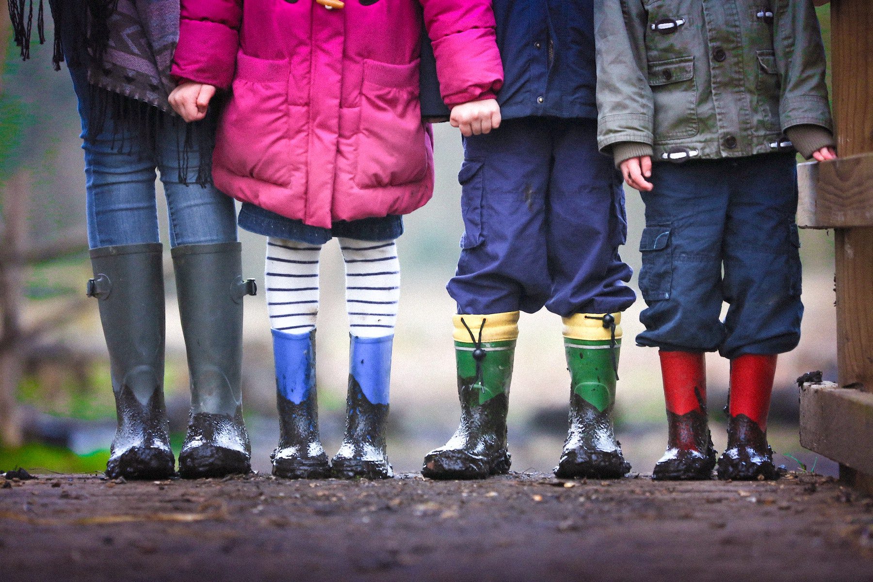 Four children in rainboots and colorful jackets hold hands, only visible up to their chests. 