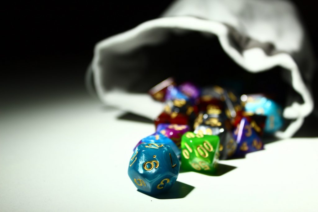 Multi-colored D20 and other dice for Dungeons and Dragons, scattered on a white table from a gray cloth bag.