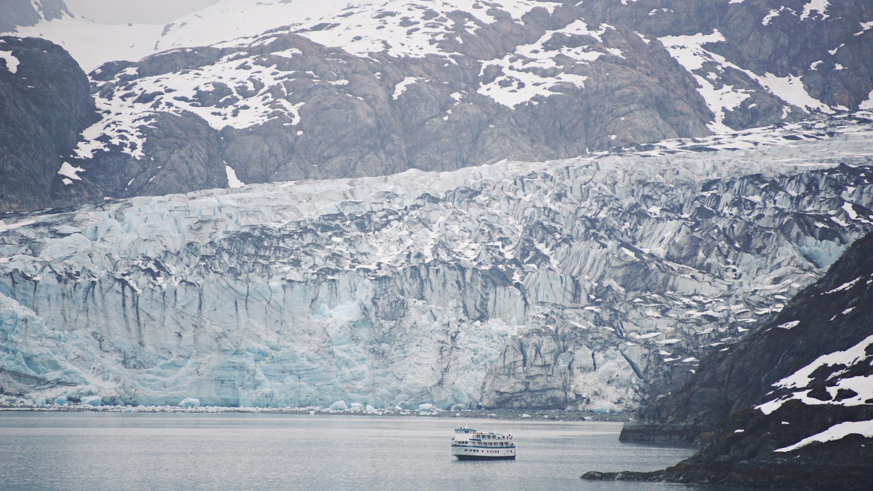 A cruise ship navigating the waters of Glacier Bay National Park in Alaska, alongside a glacier and snowy mountain.