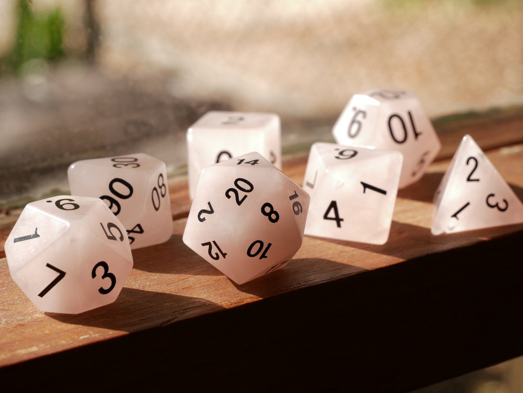 White various dice such as D20, D12, D10, and a normal 6-sided dice are laid in a sunlit window sill