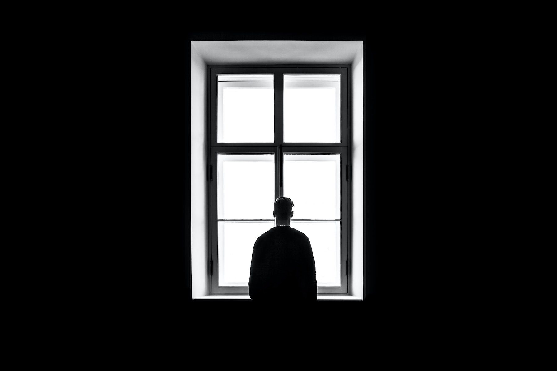 A silhouette of a man in front of a large window, black and white. 
