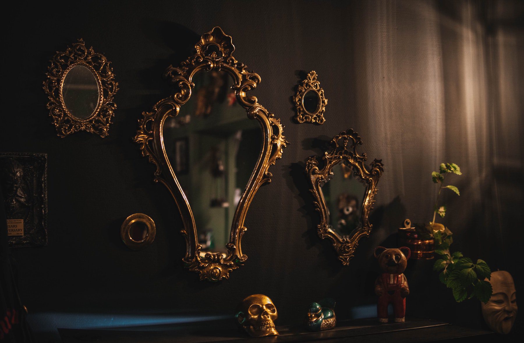 Several gold-framed antique mirrors on a black or brown wall in dim lighting. 