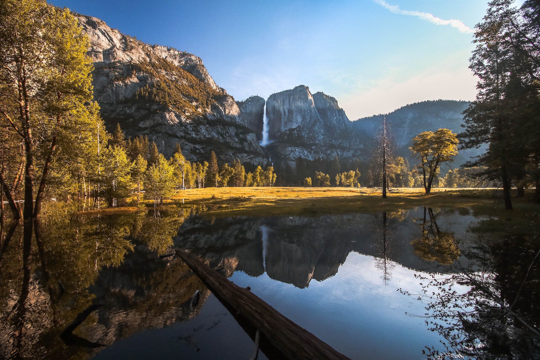 Yosemite Valley in Yosemite National, one of the most visited parks in the United States depicting a still lake reflecting the background of large cliffs and a waterfall.